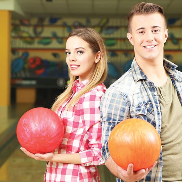 Male and female standing back to back holding bowling balls